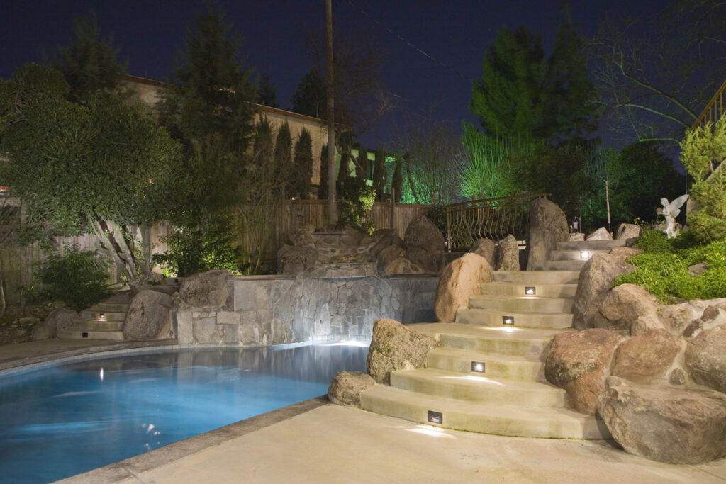 A landscape with integrated lighting surrounding a pool.