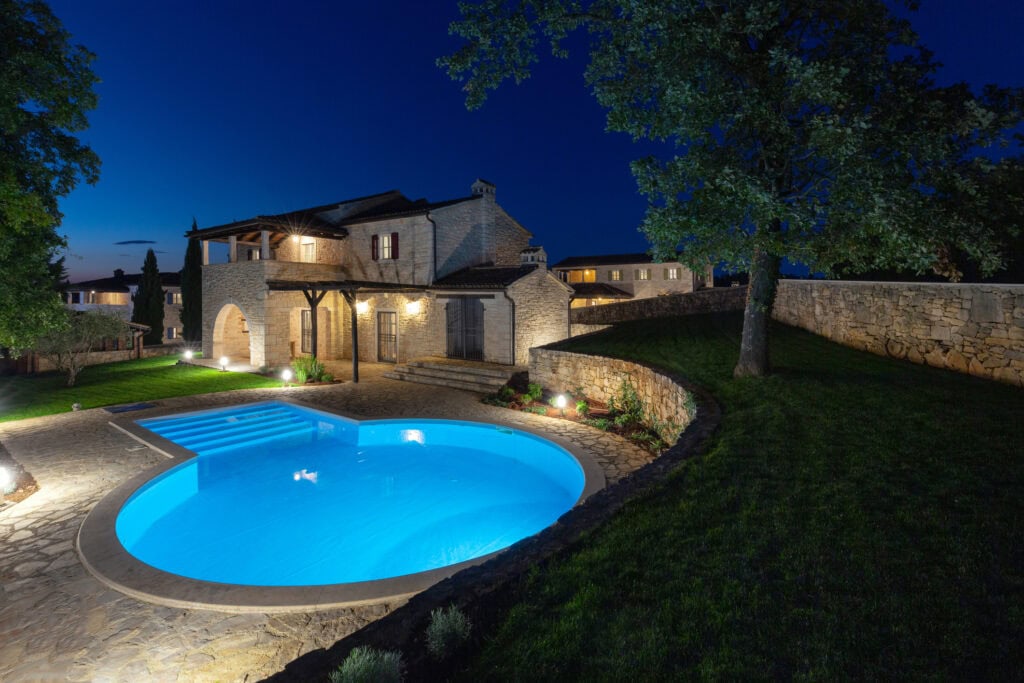 Luxury landscape lighting featuring a brightly lit pool and retaining wall at night.