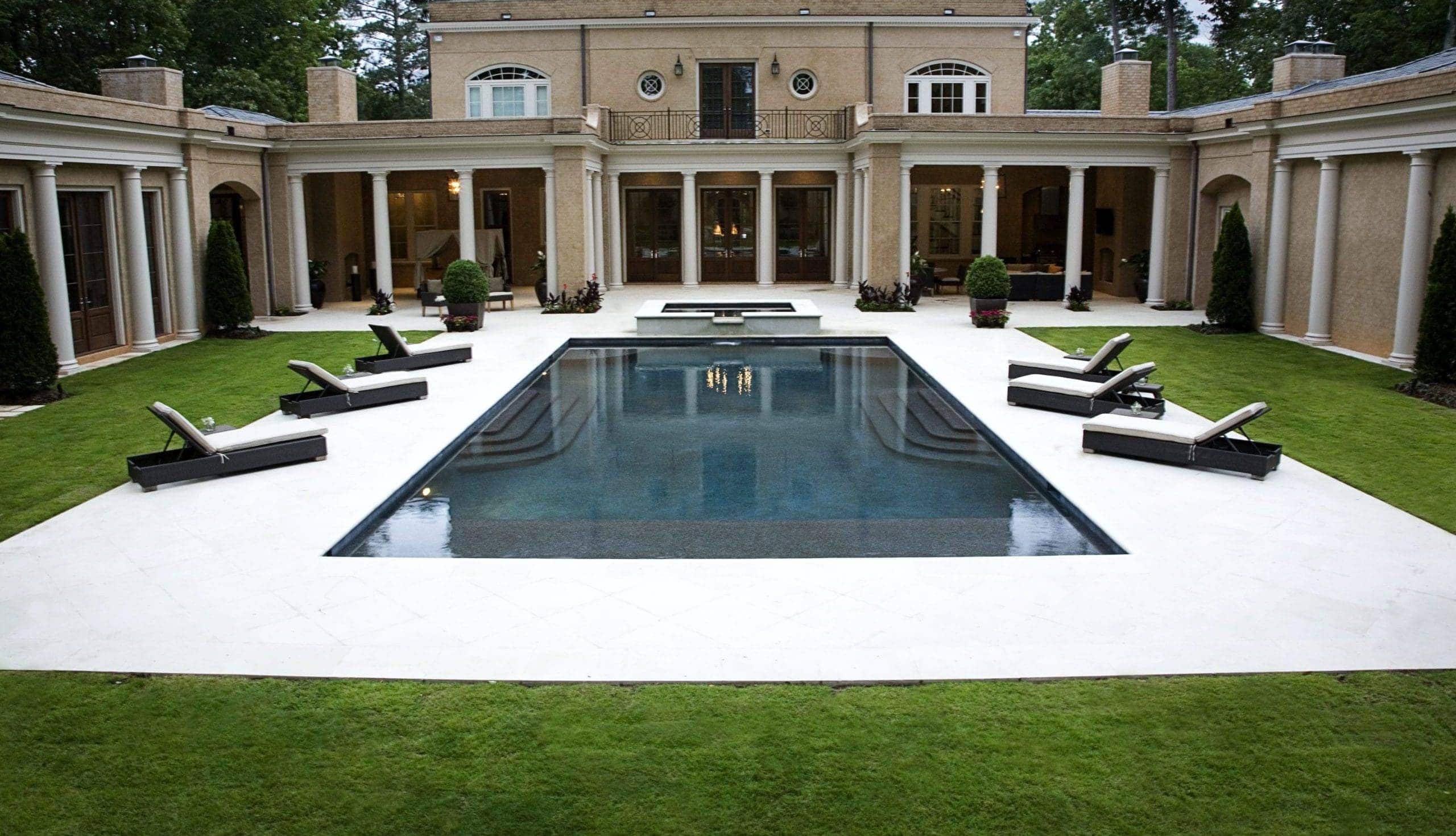 Symmetrical estate pool and courtyard with formal stone architecture and lush green lawn borders.