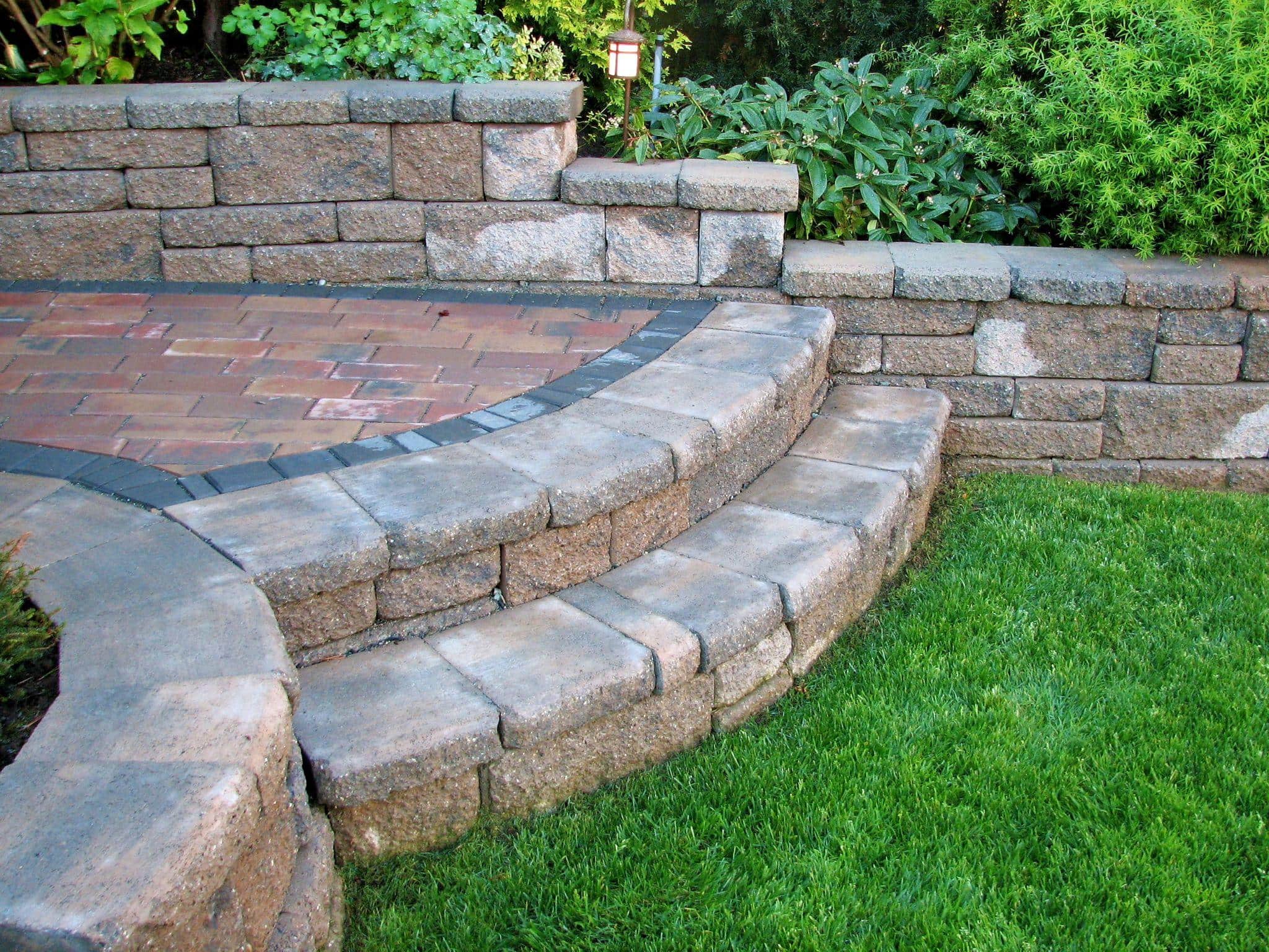 A close-up capture of 2 step footpath curved into low retaining walls on both sides built with rustic appearing blocks leading on to paving stone deck area.