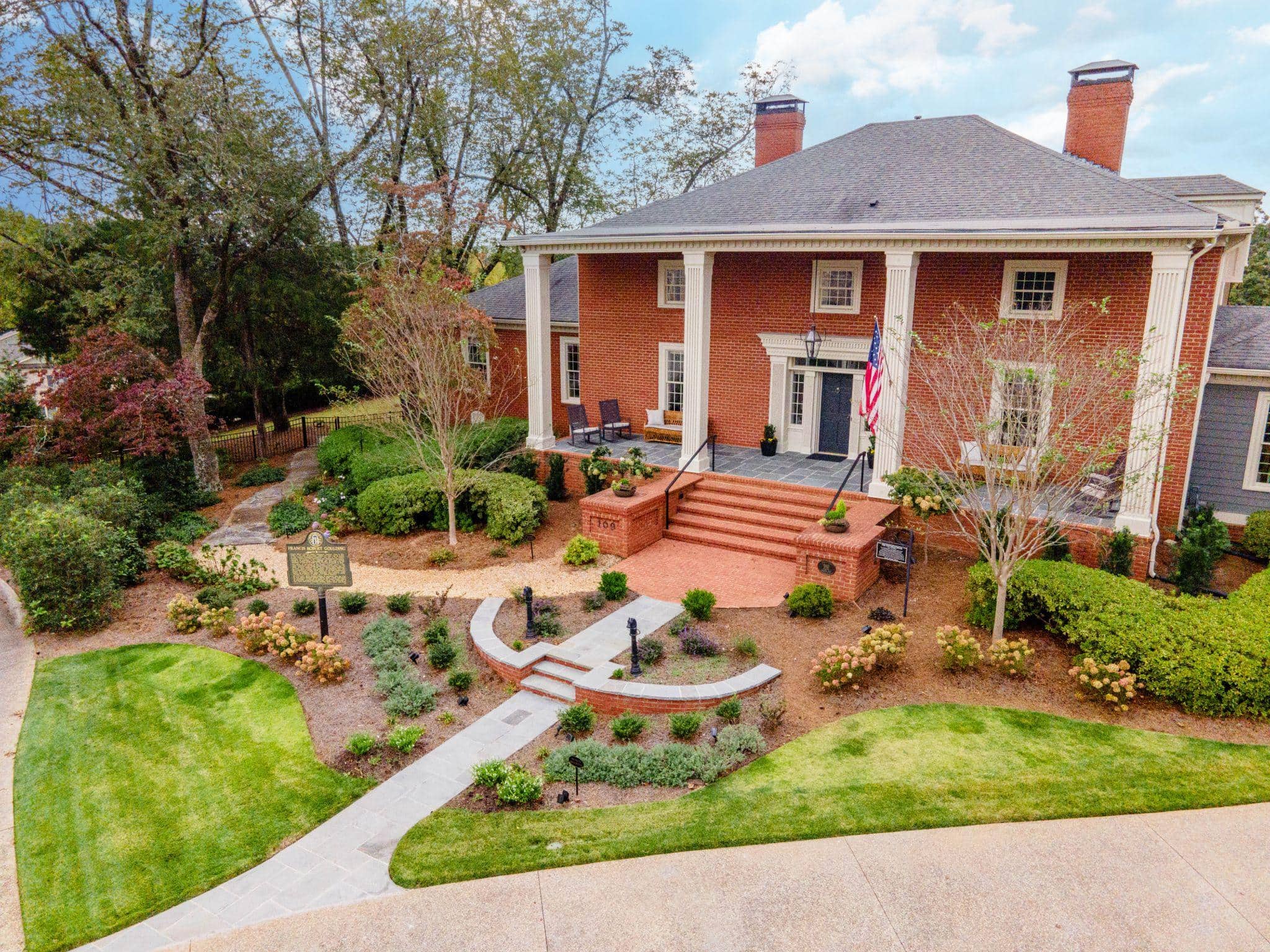 Aerial view of brick colonial home with curved walkway and formal garden beds