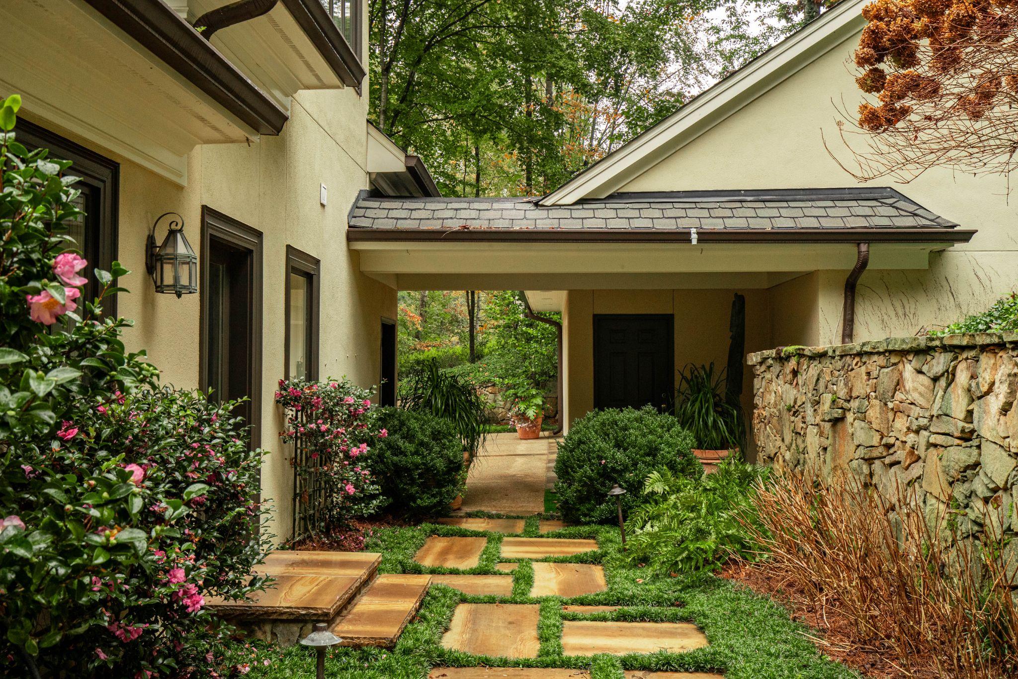 Covered side courtyard with stone wall, flowering shrubs, and stepping-stone pathway