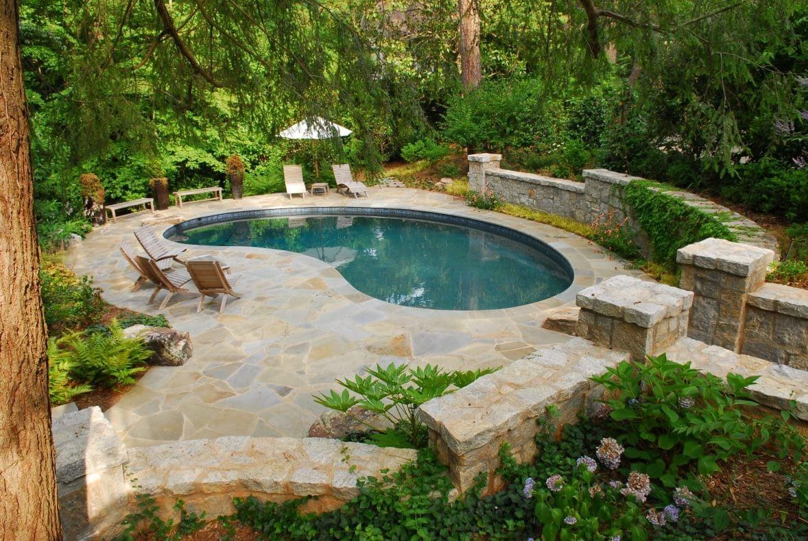 Curved natural stone pool surrounded by trees and retaining wall