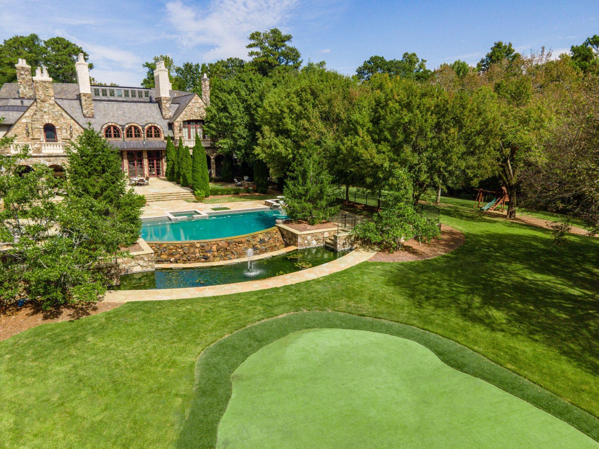 Estate backyard with pool, pond, manicured lawn, and putting green.