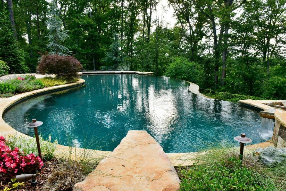 Freeform natural stone pool surrounded by mature trees and landscape lighting