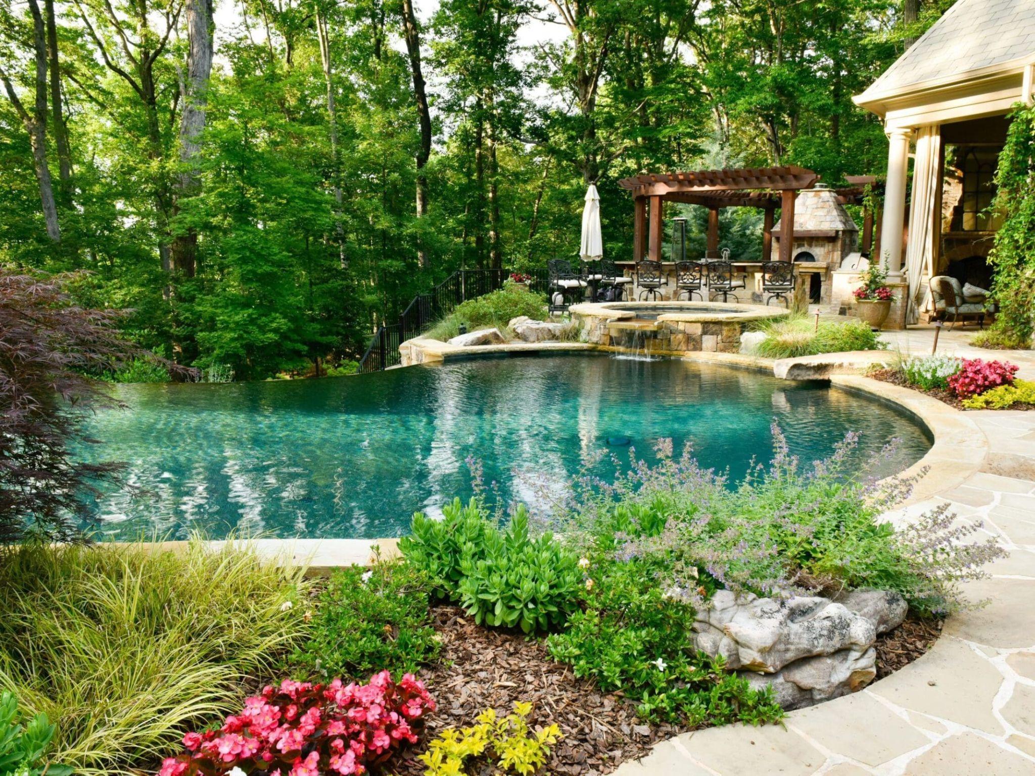Infinity-edge pool with spa, pergola, and outdoor kitchen, with a wooded backdrop