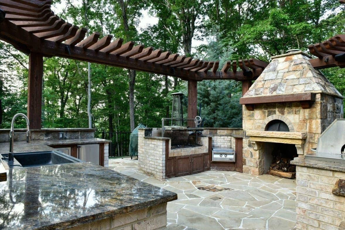Outdoor kitchen with stone pizza oven under wooden pergola.