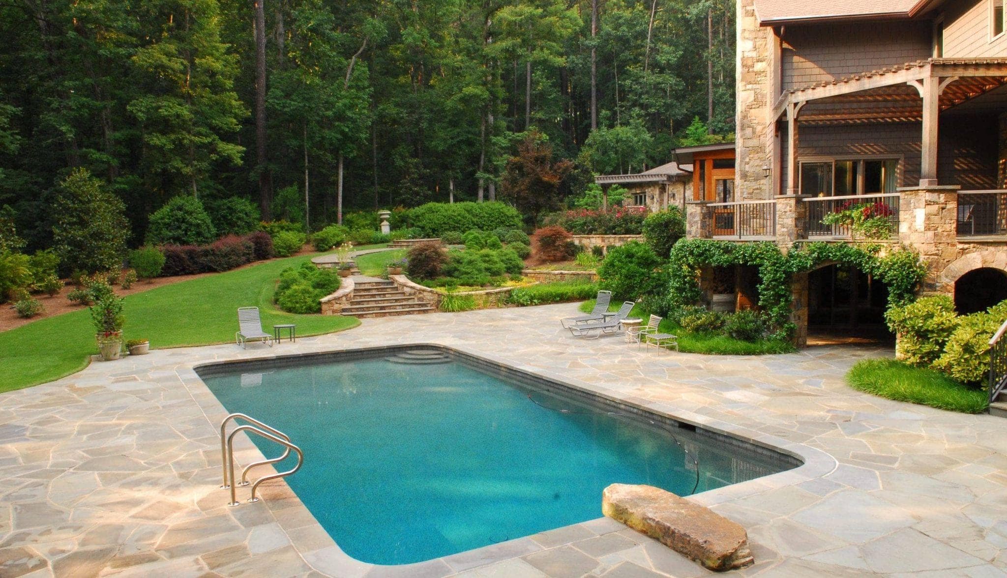 Rectangular stone pool beside luxury home with landscaped backyard